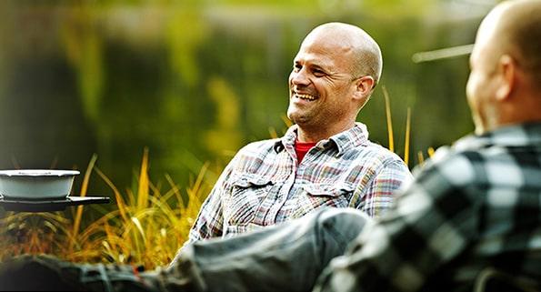 two men sitting and laughing by a pond